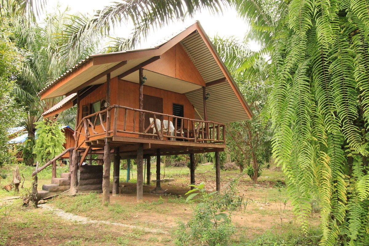 A wooden cabin with a balcony, surrounded by lush greenery.