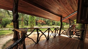 Una terraza de madera con barandilla, rodeada de abundante vegetación y vistas a un jardín.