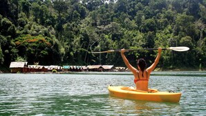 Una persona en un kayak amarillo sobre aguas tranquilas, con una orilla boscosa al fondo.