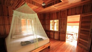 Una habitación de madera con una cama bajo una mosquitera, paredes de madera y una ventana con persianas.