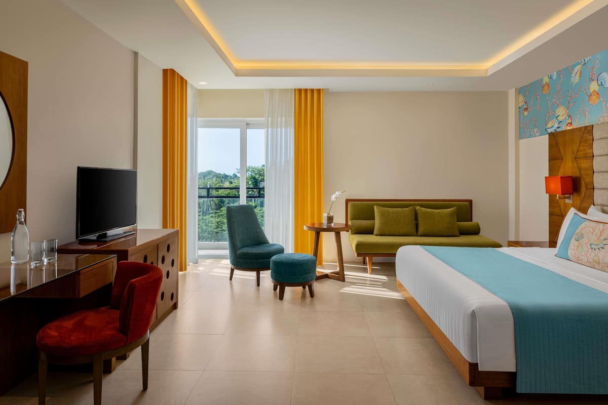 Habitación de hotel con cama, sofá, escritorio con televisor, silla y vistas al exterior.