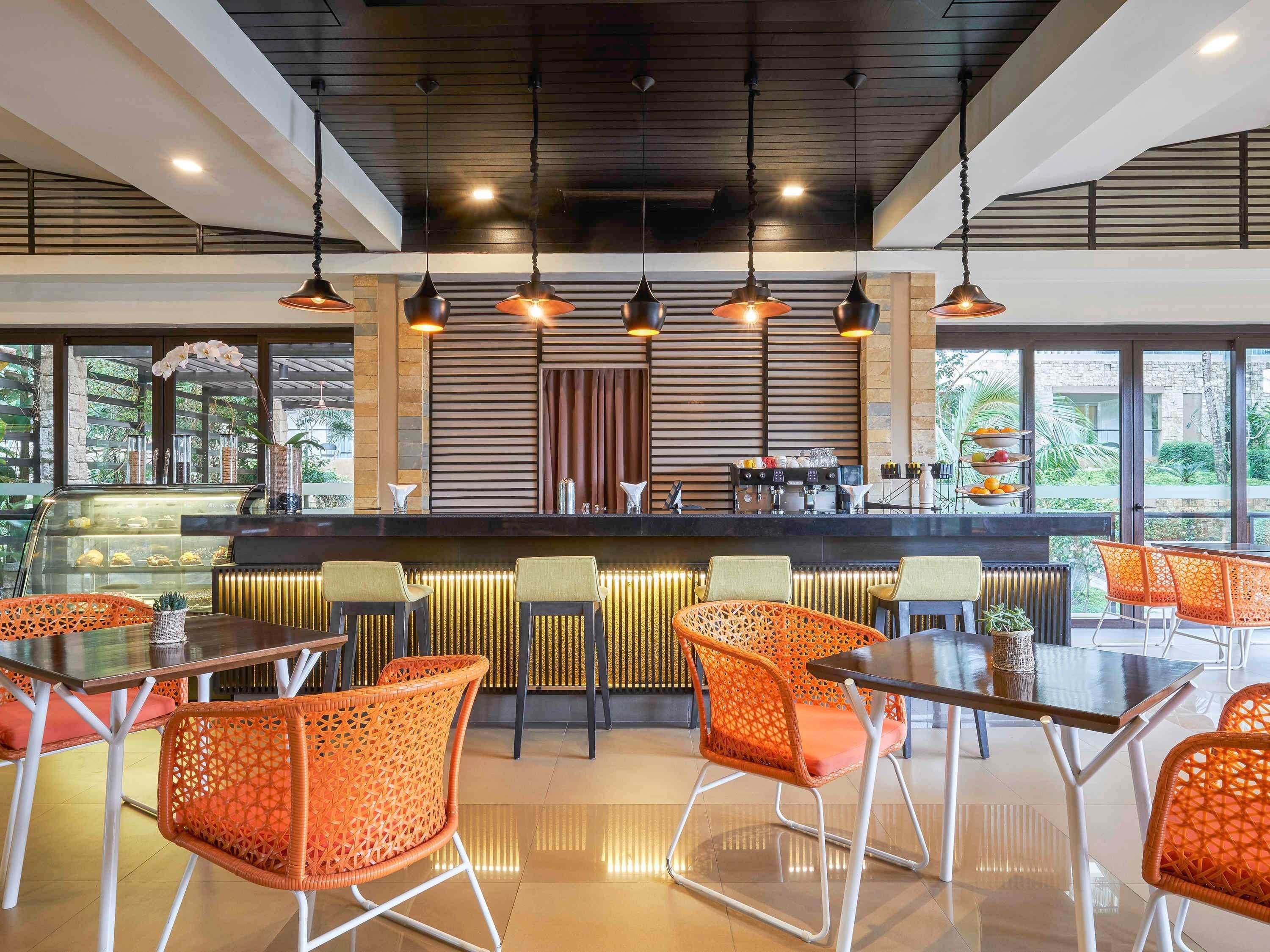 Un moderno bar con diversas opciones de asientos, una barra con cafetera y amplios ventanales con vistas al exterior.