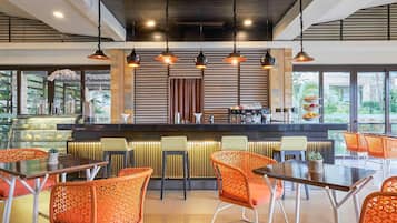 Un moderno bar con diversas opciones de asientos, una barra con cafetera y amplios ventanales con vistas al exterior.
