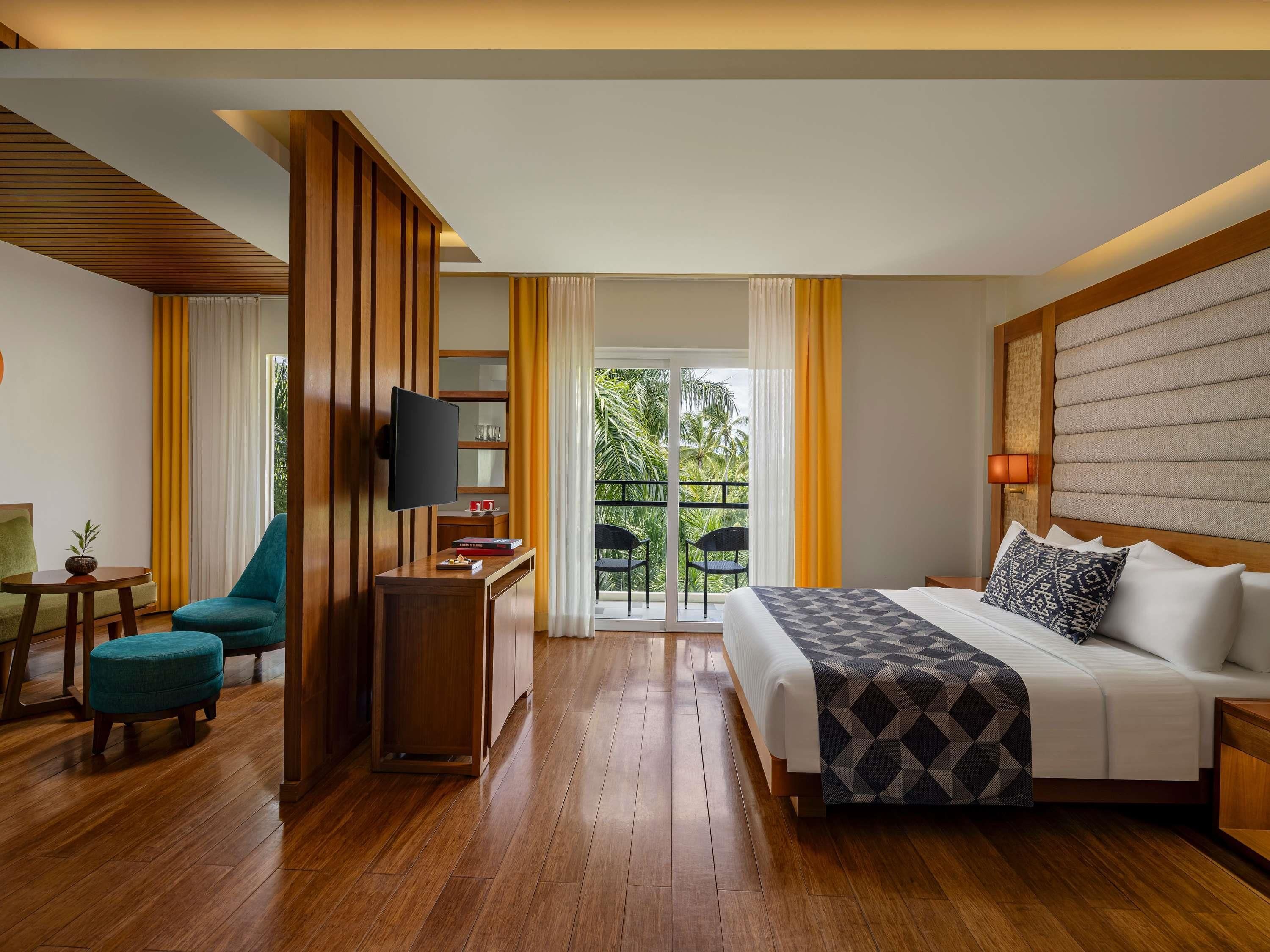 Habitación de hotel con cama, escritorio con televisor, una silla y vista al exterior.