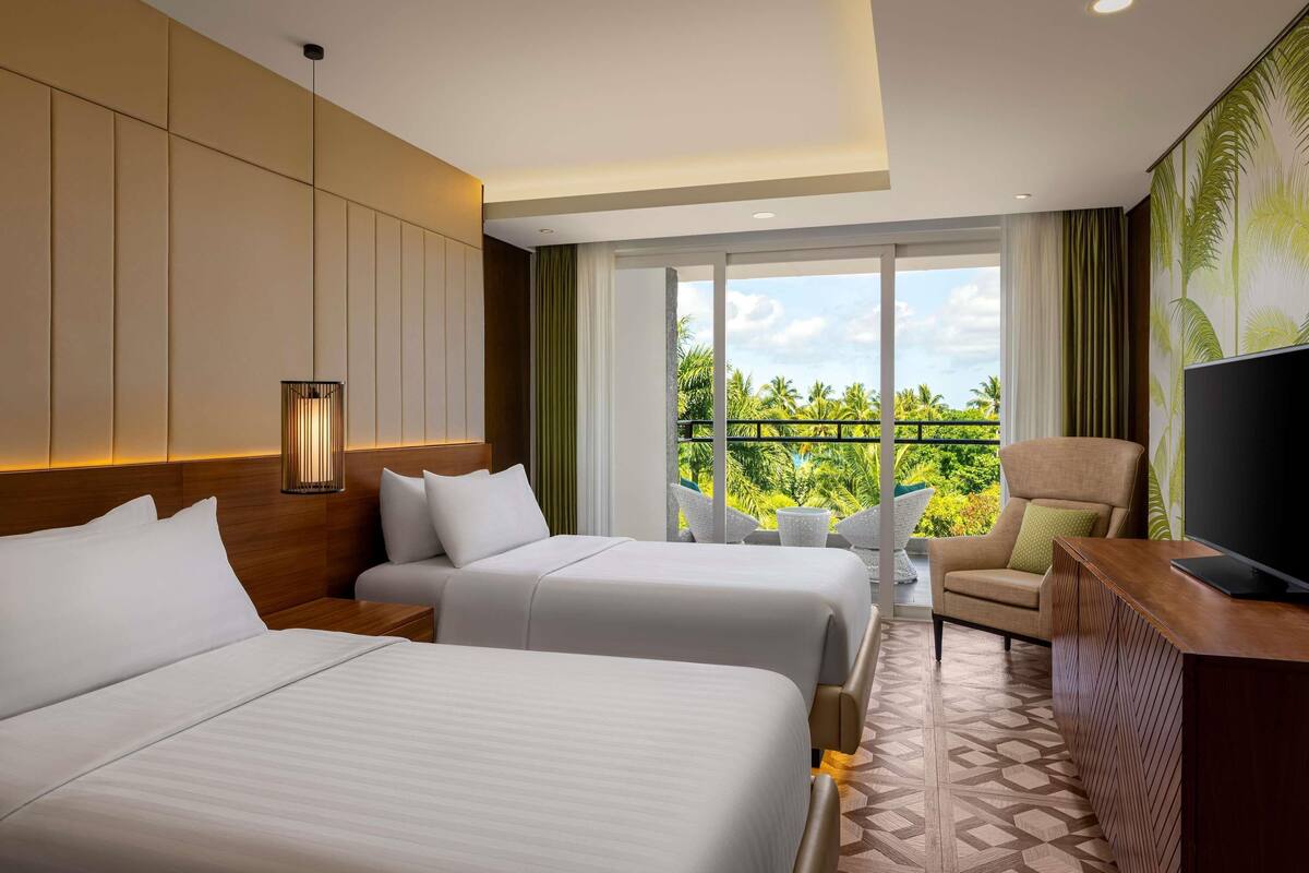 Habitación de hotel con dos camas, un televisor, un balcón y vistas a palmeras, además de un suelo con diseño.