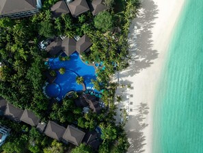 Vista aérea de un complejo turístico con una piscina grande, palmeras y una playa.