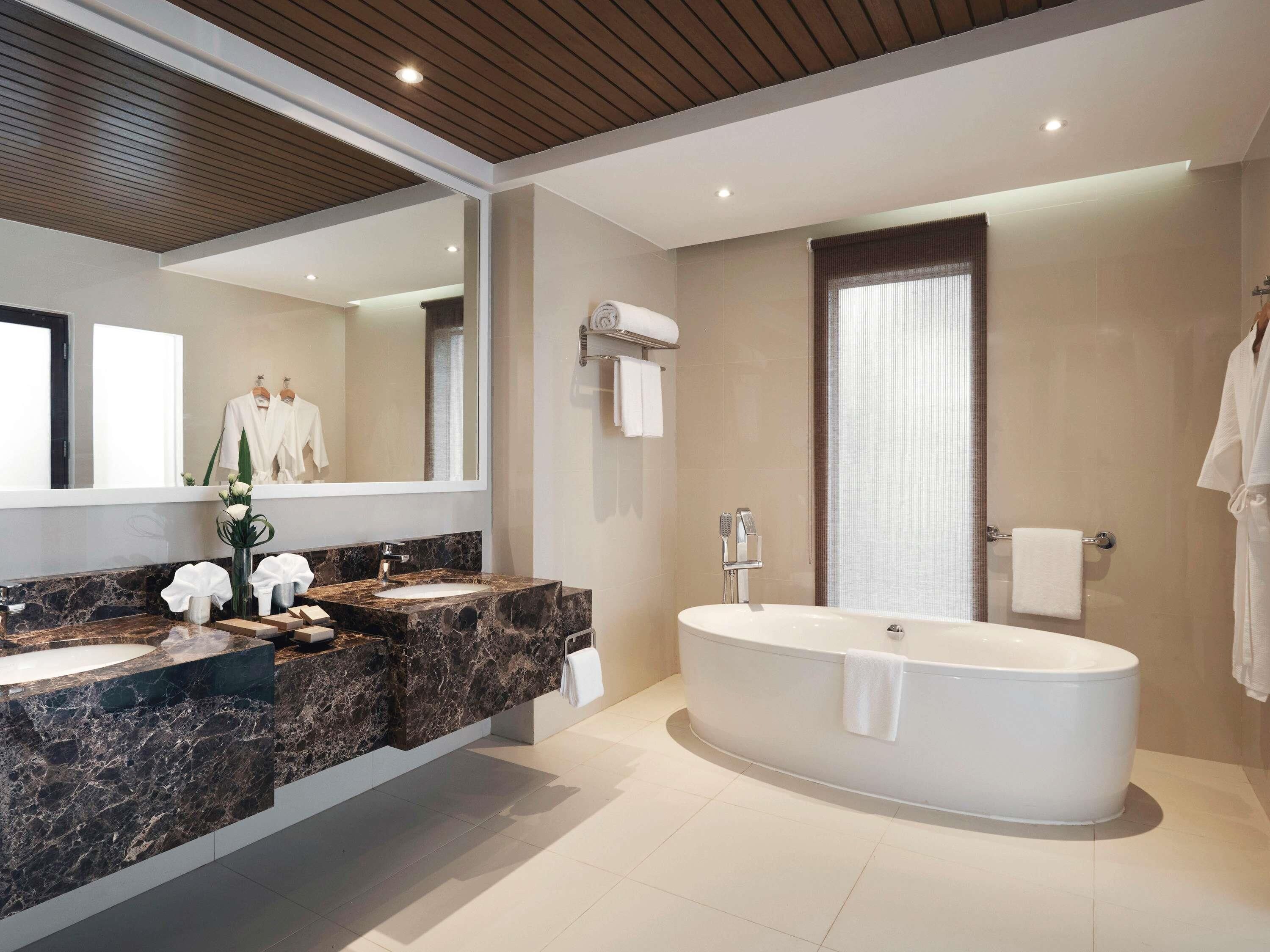 Un baño moderno con una bañera independiente, un espejo grande y un tocador de mármol.
