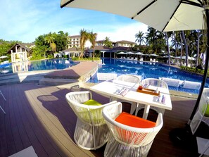 A poolside area with white wicker chairs and a table, a clear view of the pool, and a building in the background. - Mövenpick Resort & Spa Boracay (Boracay Island)