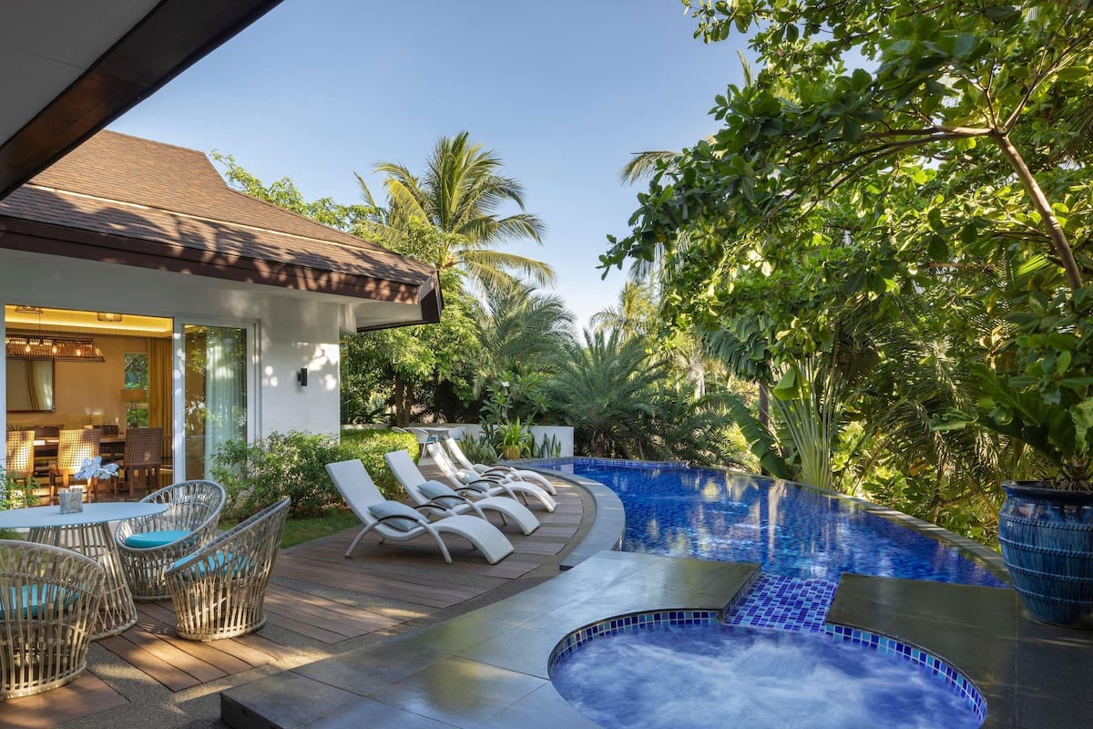 Un área de piscina con sillones de descanso, un jacuzzi y un comedor con mesas al aire libre.