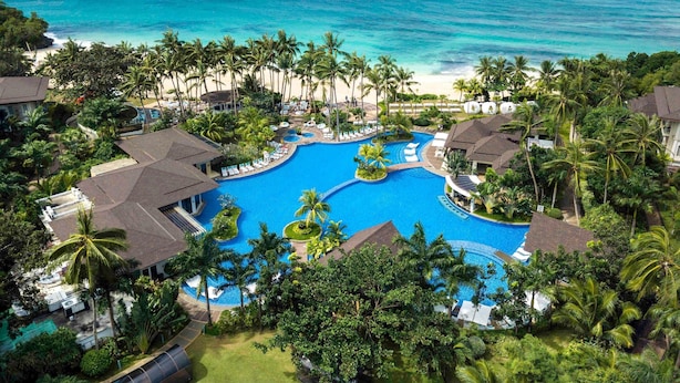 A resort with a large central pool, surrounded by palm trees and beachfront views. - Mövenpick Resort & Spa Boracay (Boracay Island)