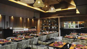 A restaurant with multiple tables, wicker chairs, and hanging light fixtures.