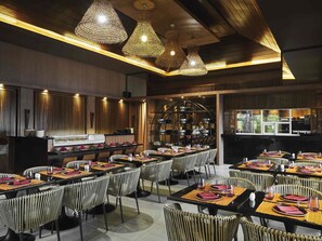 Un restaurante con varias mesas, sillas de mimbre y lámparas colgantes.