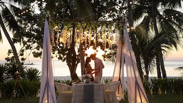 Ambiente tropical ao ar livre com toldo, luzes de corda e uma mesa com cadeiras.