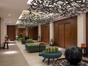 A modern lobby with a high ceiling, wooden paneling, and a unique ceiling installation of hanging elements. There are seating areas with cushions and a decorative water feature. - Mövenpick Resort & Spa Boracay (Boracay Island)