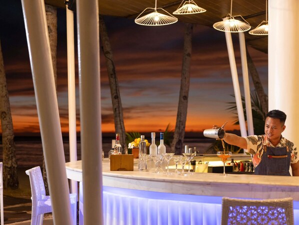 Un espace bar offrant une vue sur le coucher de soleil, doté de tabourets et d’une variété de bouteilles et de verres.