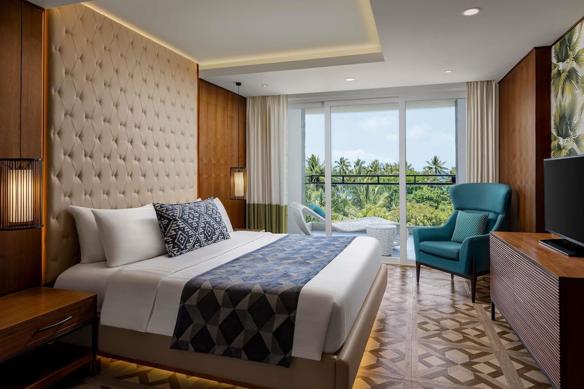 Una habitación de hotel moderna con una cama grande, un escritorio, una silla y un balcón con vistas a palmeras.