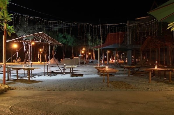 An outdoor area with tables and chairs, string lights, and a covered structure.