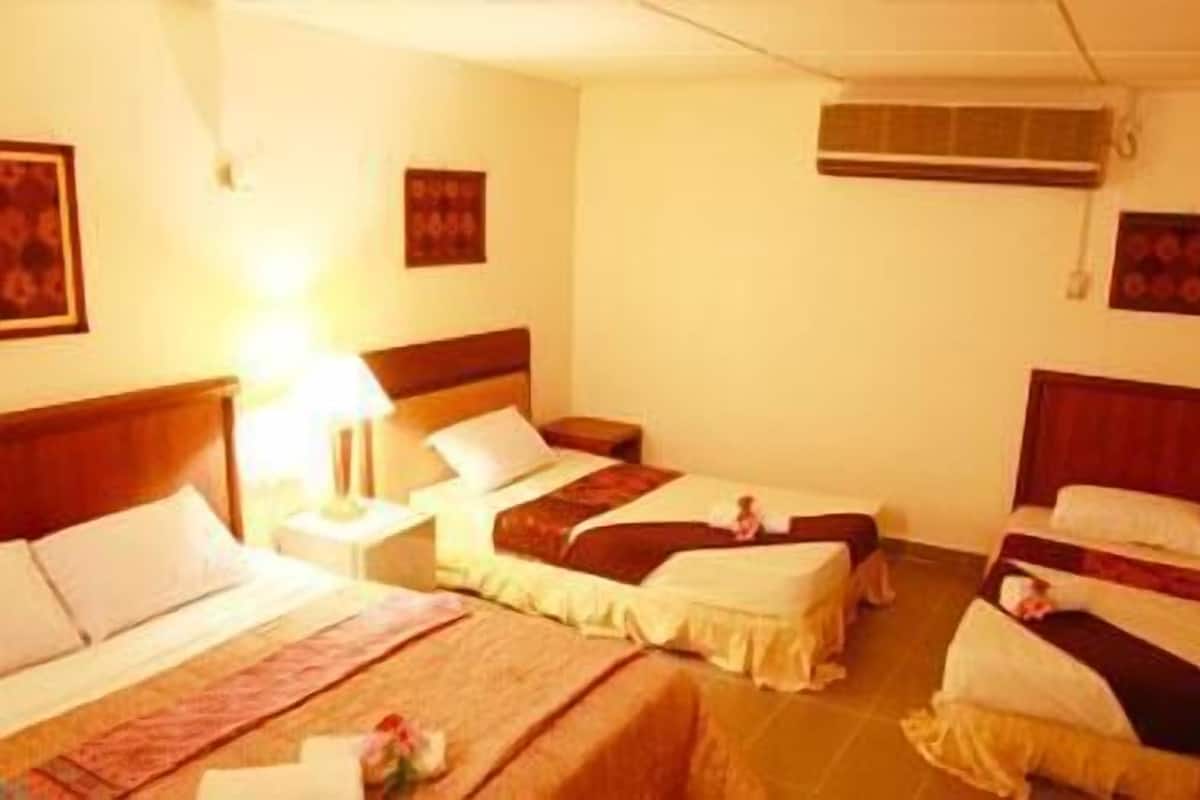 A hotel room with three single beds, a nightstand with a lamp, and an air conditioning unit.