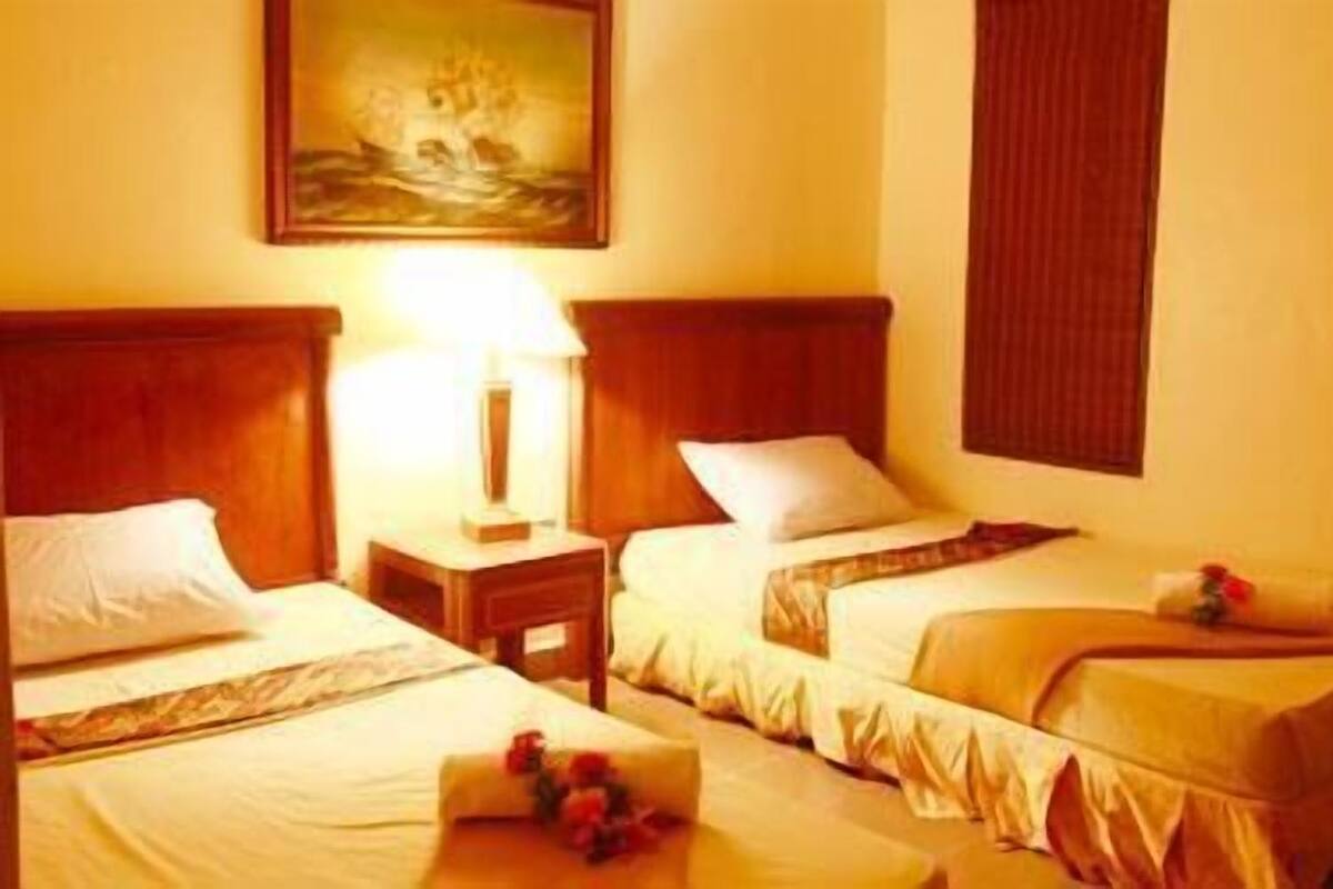 A hotel room with two single beds, a nightstand with a lamp, and a painting on the wall.