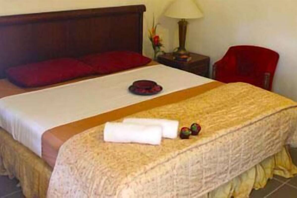 A neatly made bed with a red pillow, a white towel, and a small tray.
