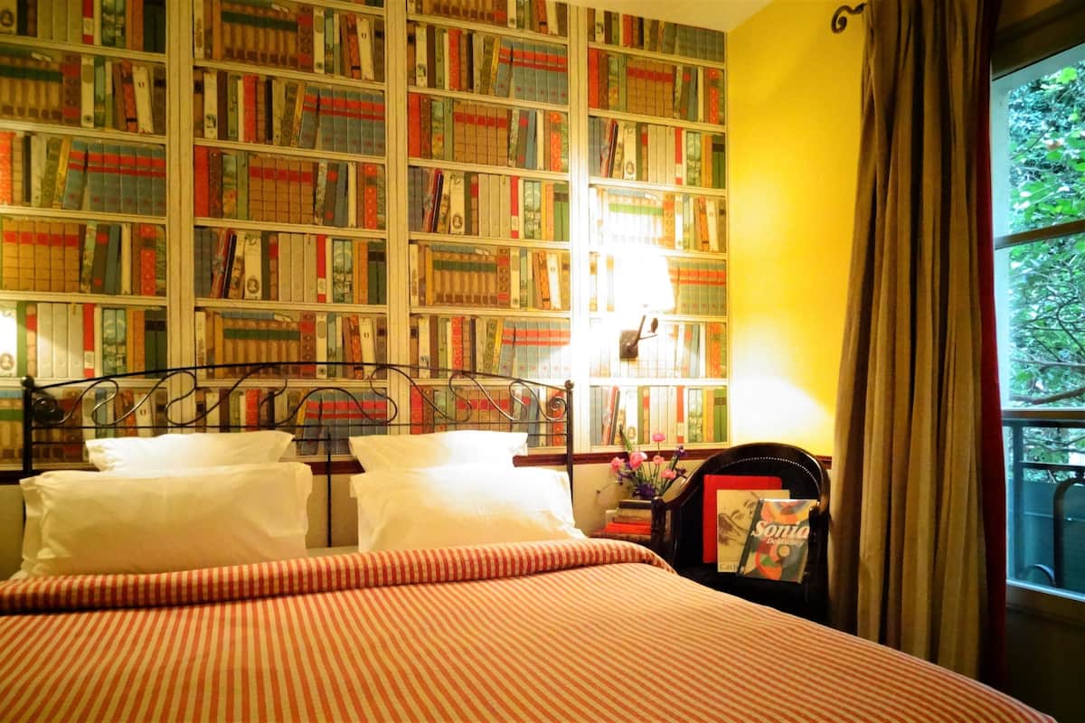 Un dormitorio con una amplia estantería, una cama con ropa de cama a rayas y una ventana con cortinas.