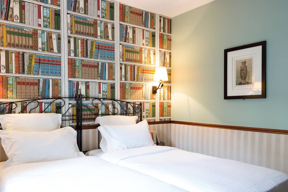 Habitación de hotel con una amplia estantería llena de libros, una cama con sábanas blancas y un cuadro en la pared.