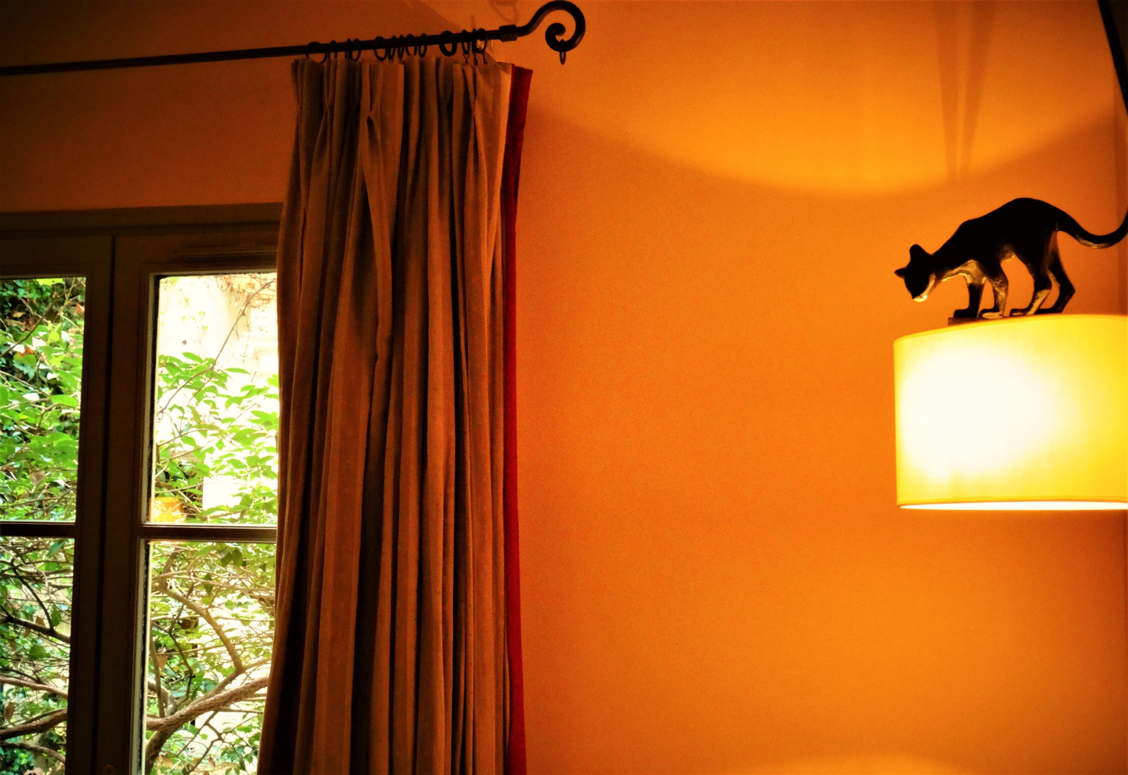 A room with a window, curtains, and a wall-mounted lamp with a silhouette of a cat.