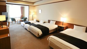 Une chambre d’hôtel avec trois lits, un bureau avec un téléphone, une chaise et un téléviseur.