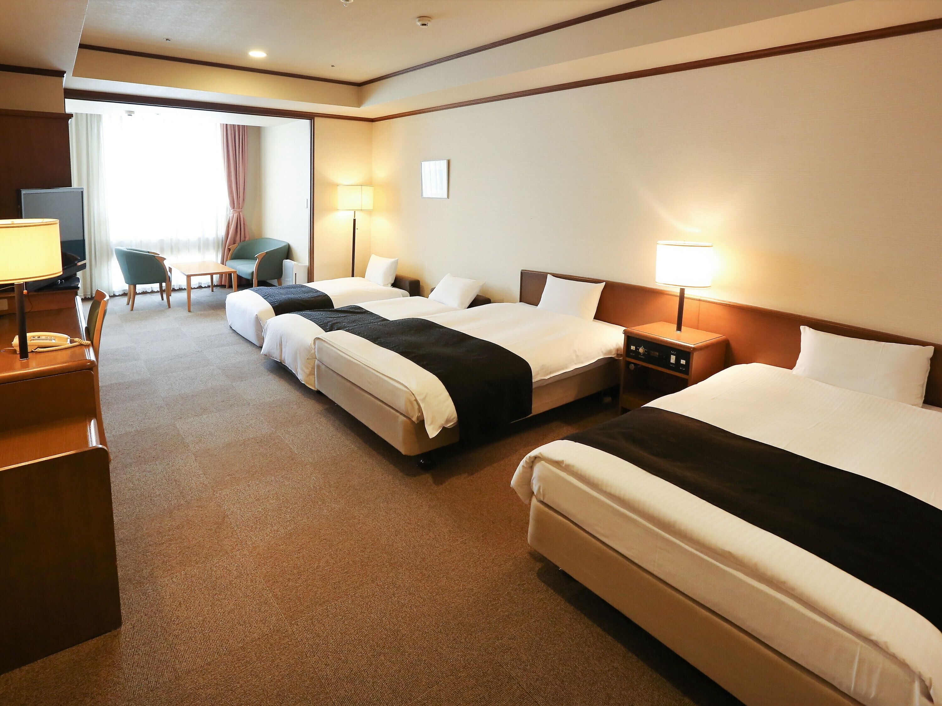 A hotel room with three beds, a desk with a telephone, a chair, and a TV.