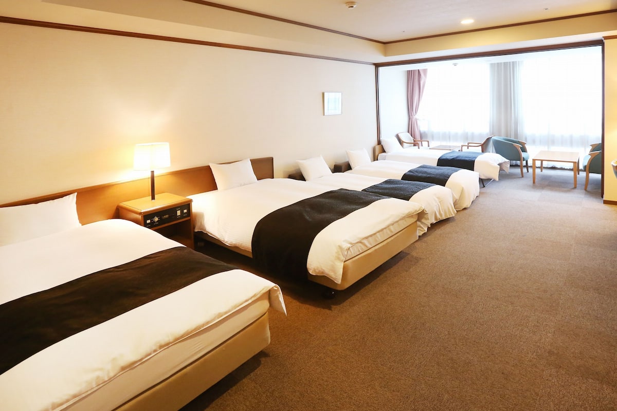 A hotel room with three beds, a desk, and a chair.