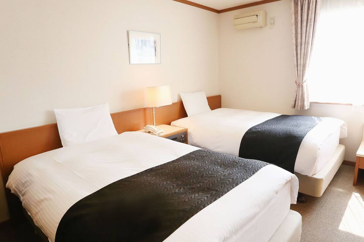 A hotel room with two beds, a bedside table with a lamp, a phone, and a picture on the wall.