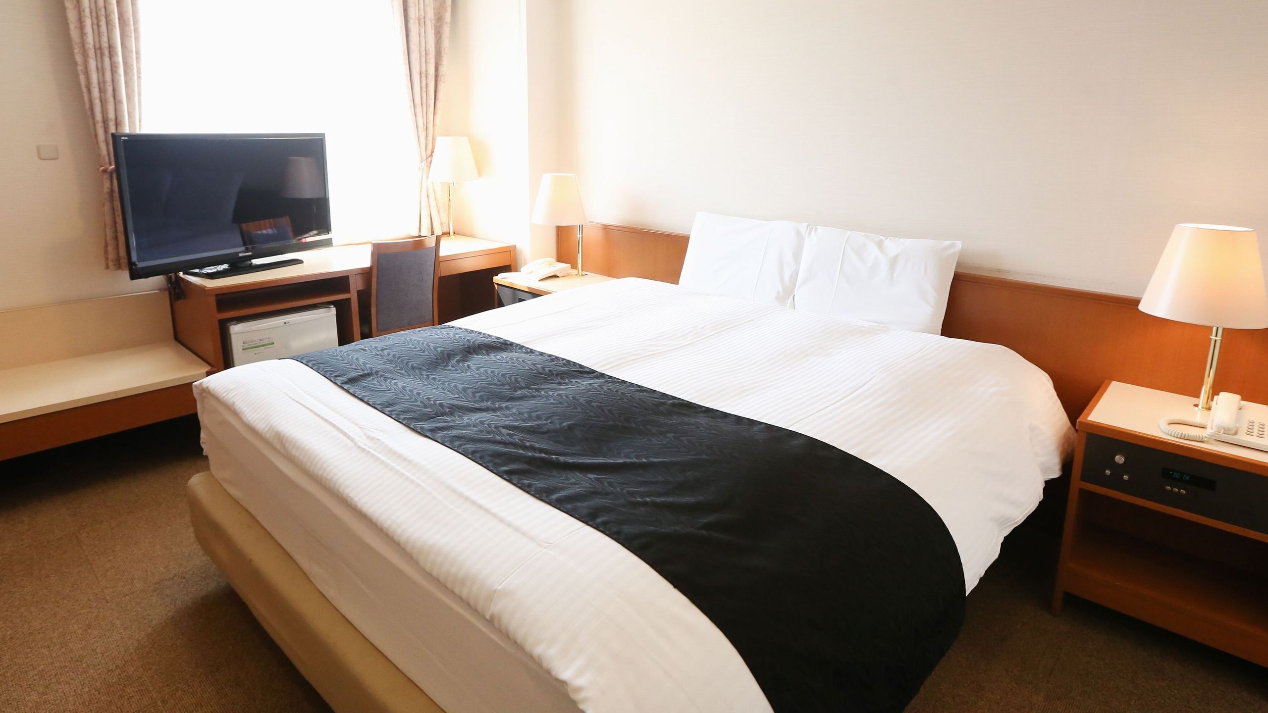 Ein Hotelzimmer mit Bett, Schreibtisch, Fernseher, Lampe, Telefon und kleinem Kühlschrank.