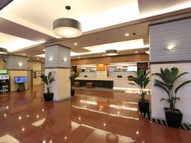 Un vestíbulo de hotel moderno con mostrador de recepción, cajero de cambio de divisas y plantas en macetas.