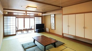 Une pièce de style japonais traditionnel, avec un sol recouvert de tatamis, une table basse, un téléviseur et des portes coulissantes donnant sur un balcon.