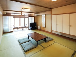 Una habitación japonesa tradicional con suelo de tatami, una mesa baja, un televisor y puertas correderas que dan a un balcón.