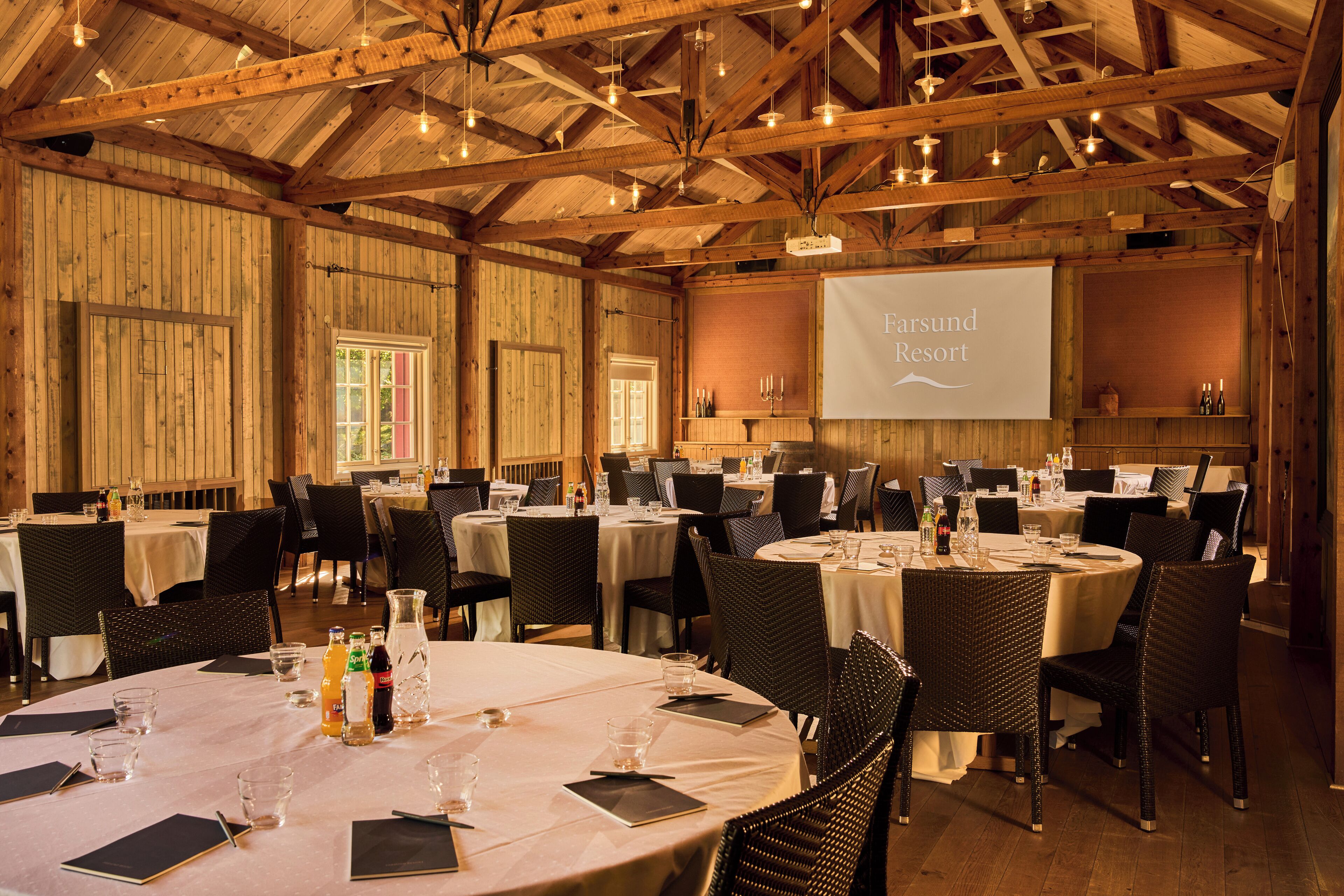 A large conference room with multiple round tables, each set with chairs, glasses, and bottles.