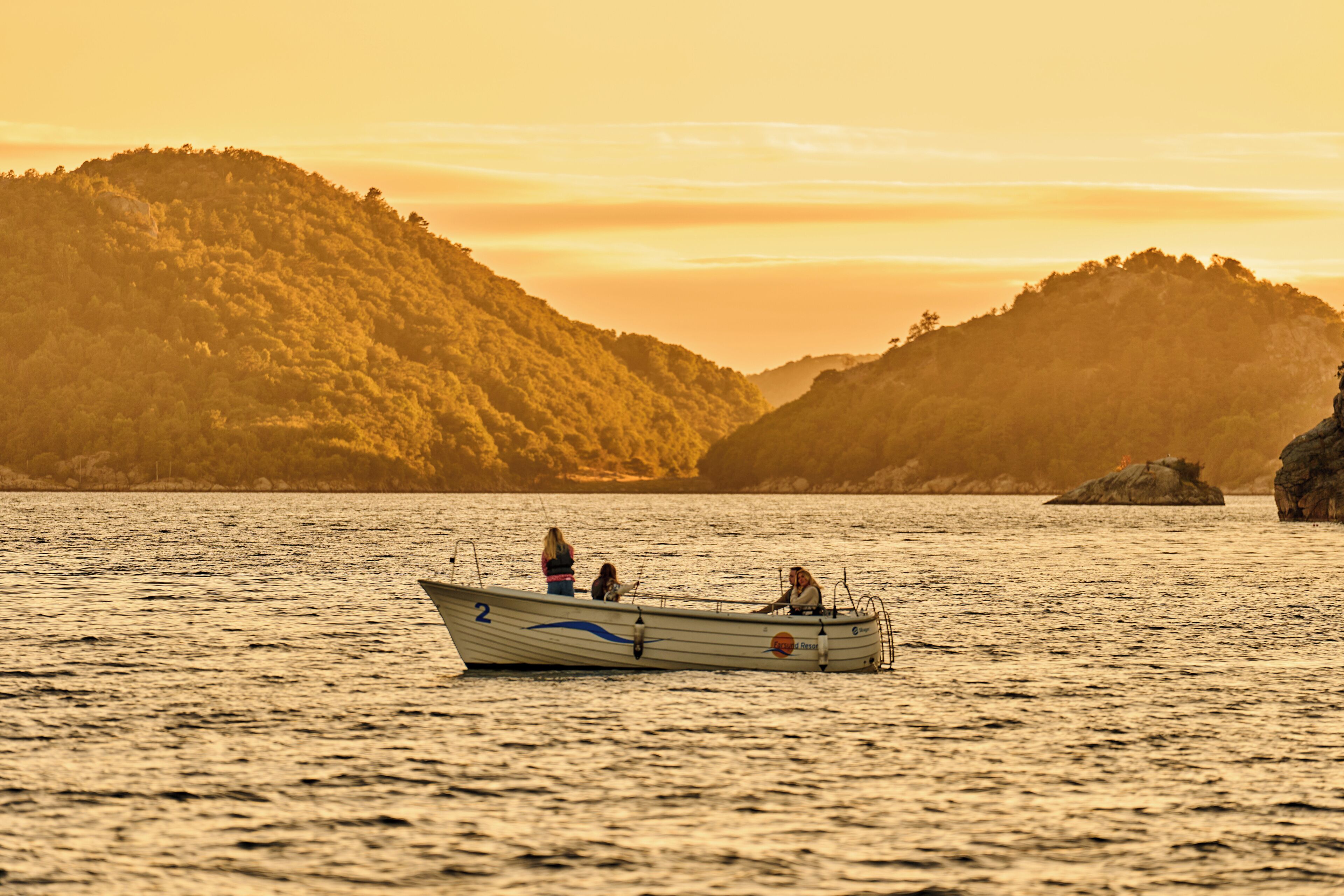 A boat with three people on a calm lake surrounded by hills.