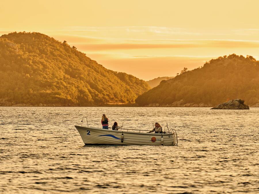 Een boot met drie personen op een rustig meer, omringd door heuvels.
