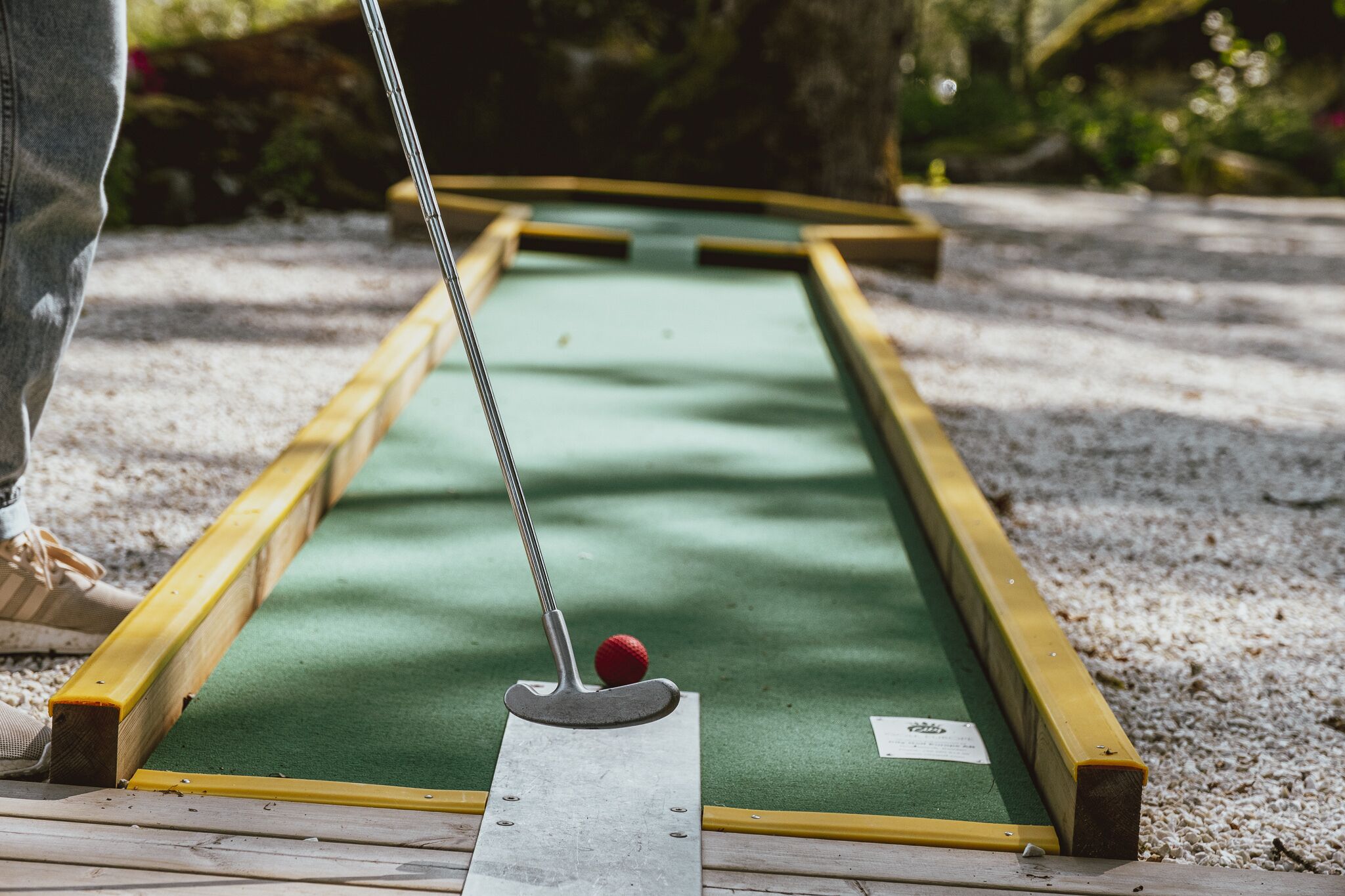 A miniature golf course with a green putting surface, wooden borders, and a metal golf club.