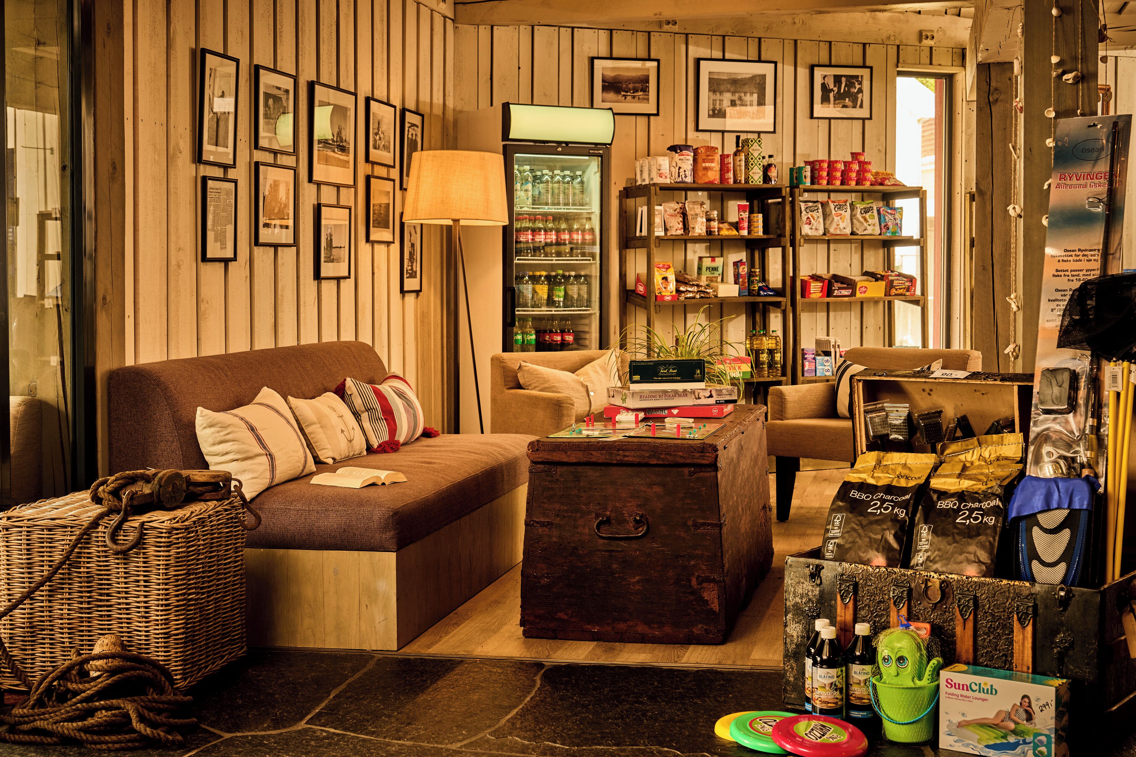 A cozy room with a sofa, a chest of drawers, a lamp, a refrigerator, and a variety of items on shelves.
