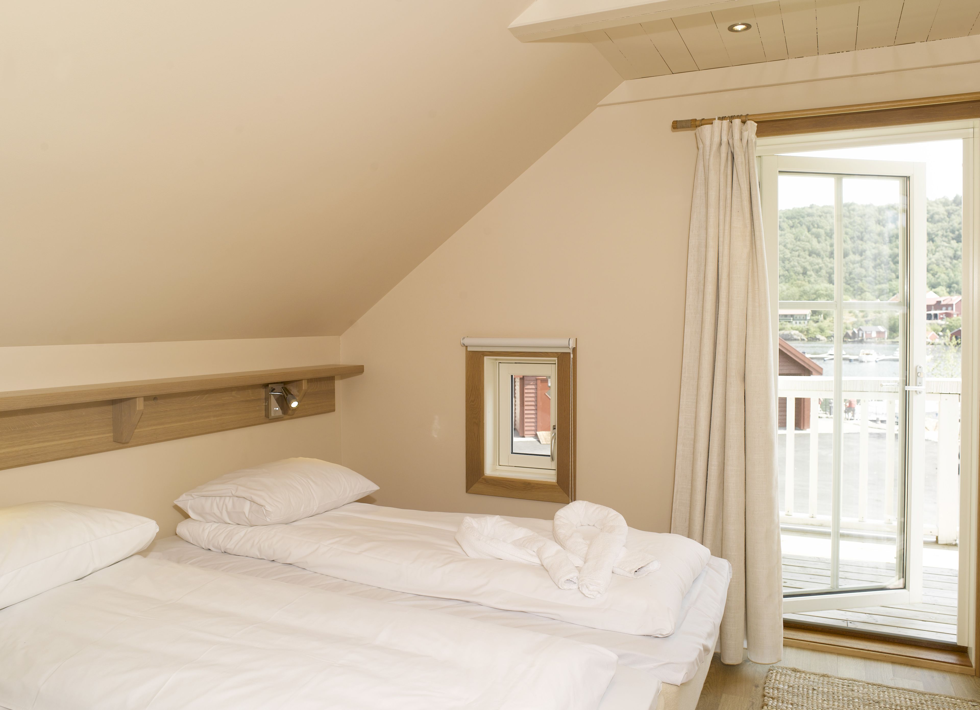 A bedroom with a bed, a window with curtains, and a view of a balcony.