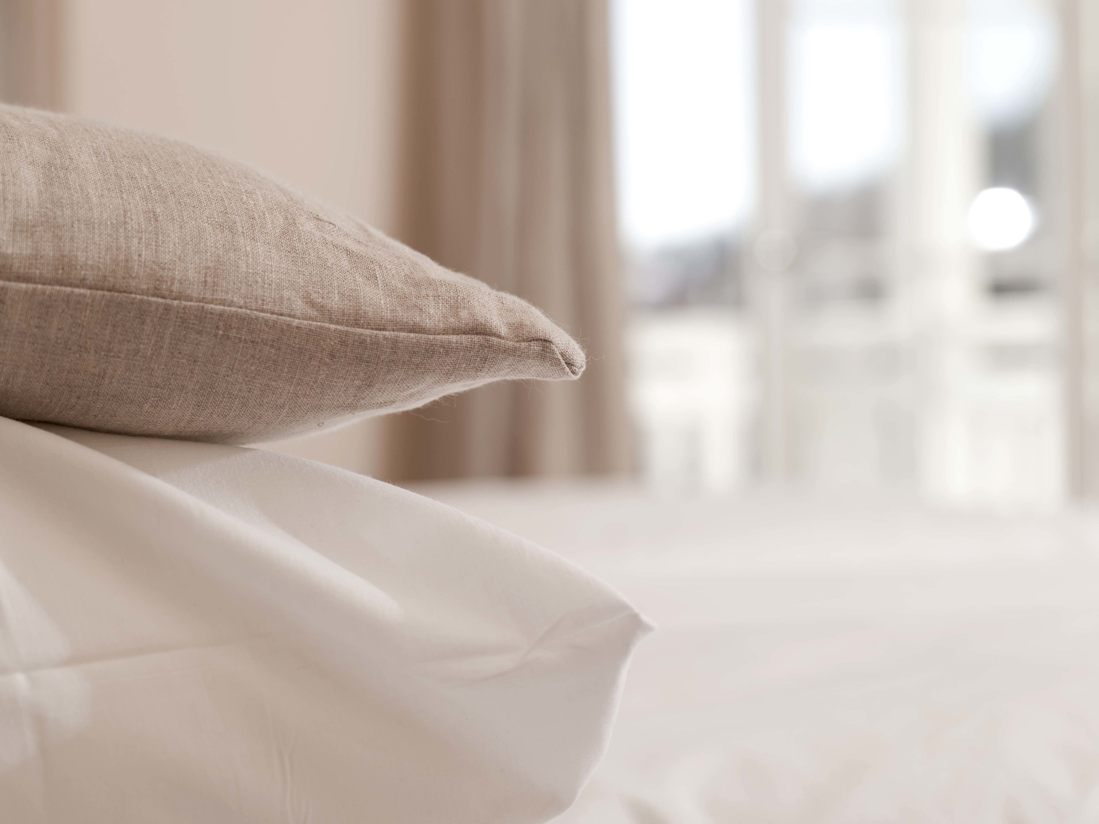 Primer plano de una cama con un almohadón color beige y sábanas blancas.