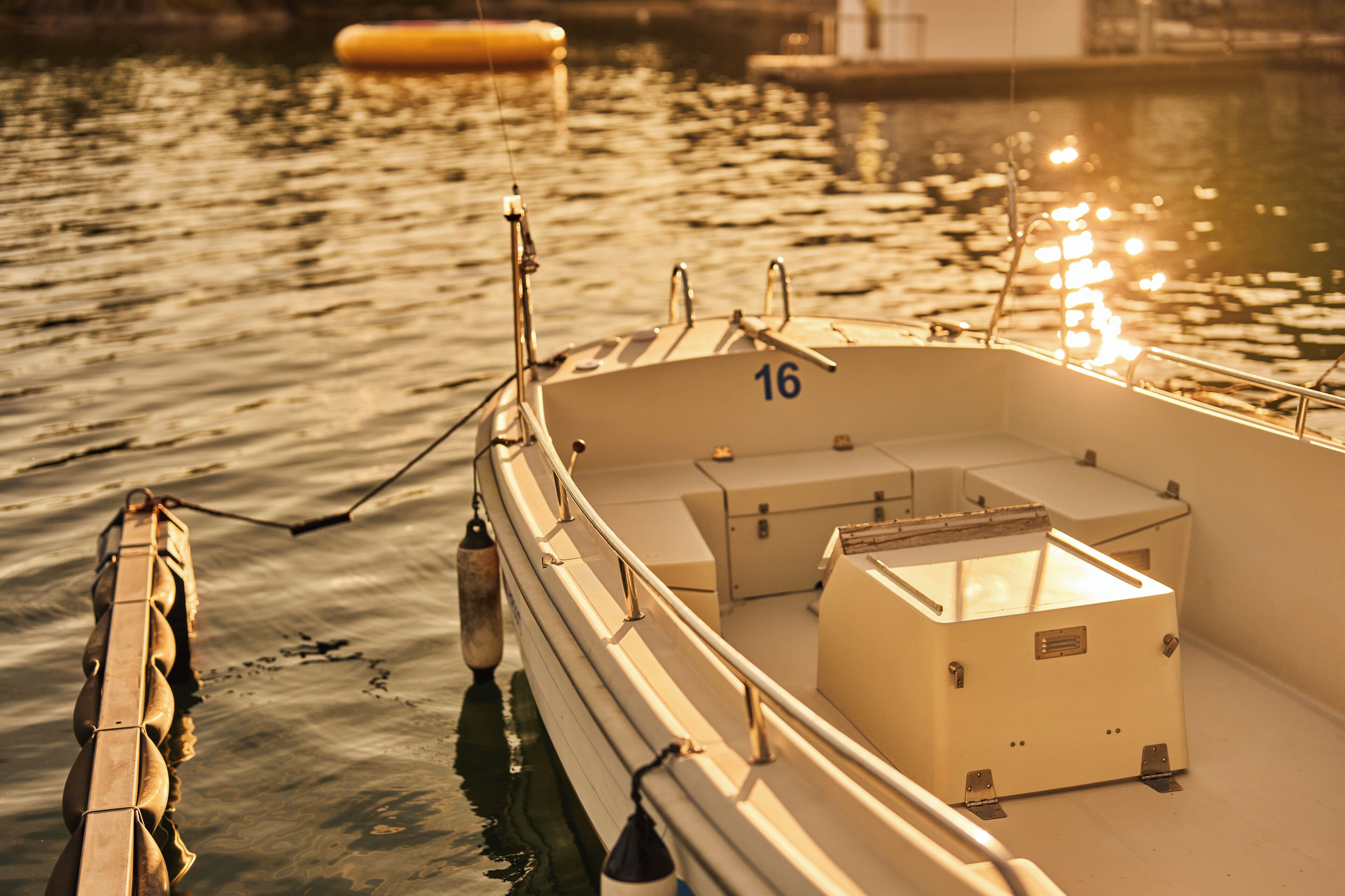 A boat with the number 16, moored at a dock with calm water and a buoy in the background.