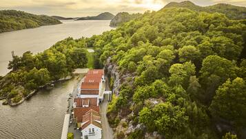 A coastal property with a white building featuring a red roof, surrounded by lush greenery and a body of water.