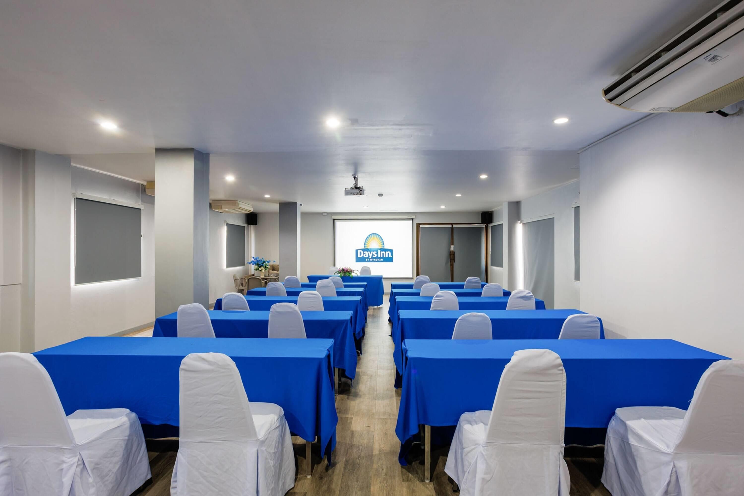 A conference room with rows of tables, white chairs, and a projector screen displaying 'Days Inn.'