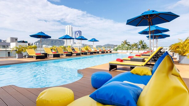 A poolside area with lounge chairs and umbrellas, a wooden deck, and a view of buildings in the background. - Days Inn by Wyndham Patong Beach Phuket (Patong)