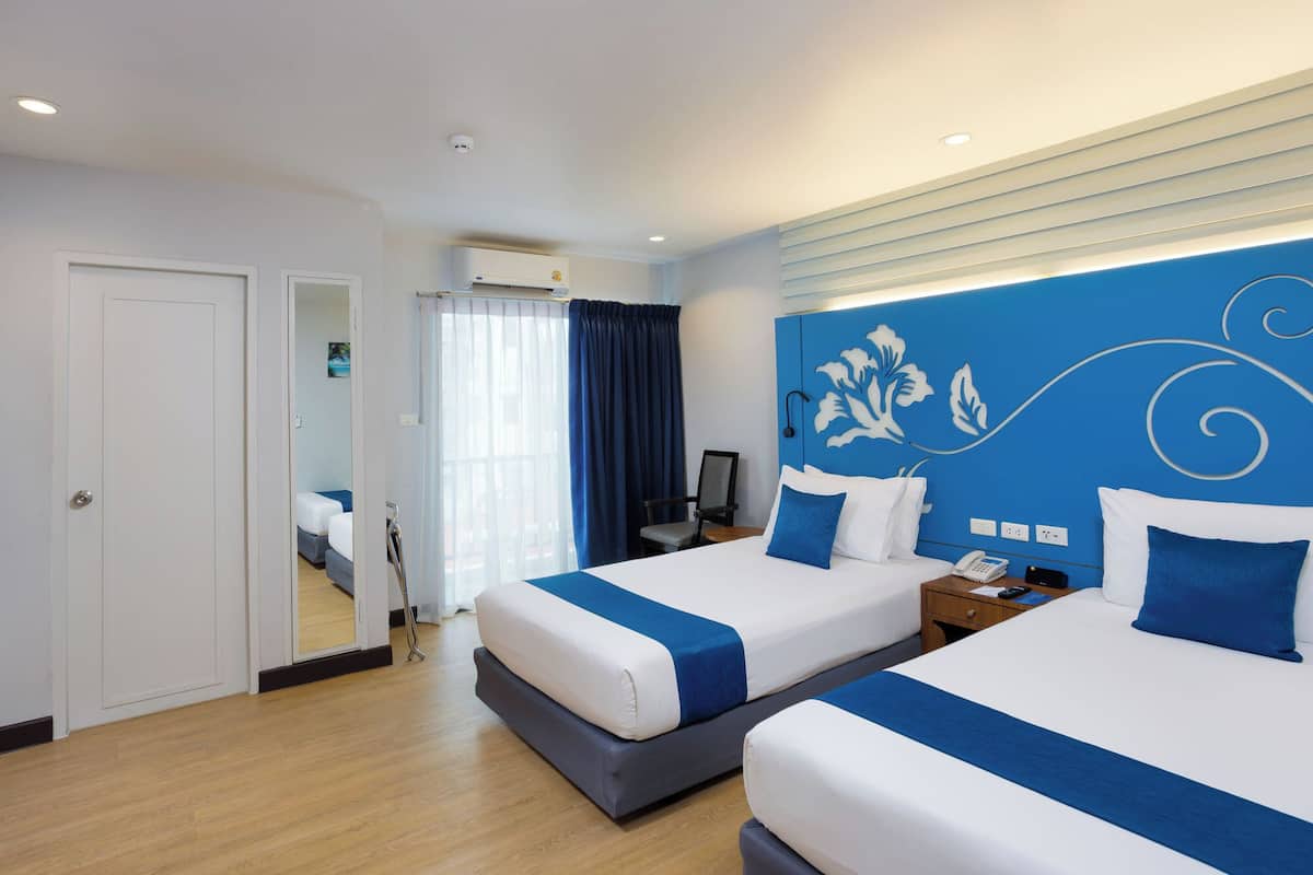 A hotel room with two beds, a desk, a chair, and a large window with curtains.