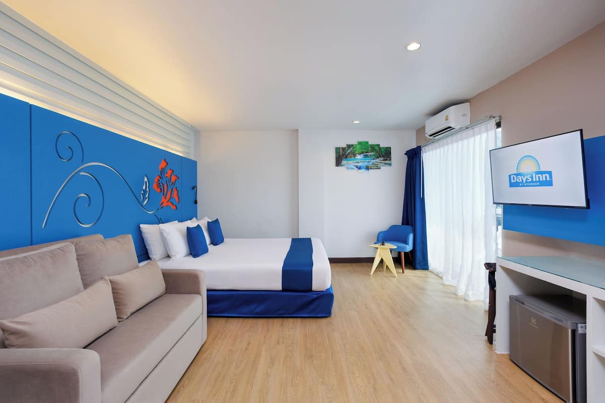 A hotel room with a bed, a sofa, a TV, and a kitchenette.