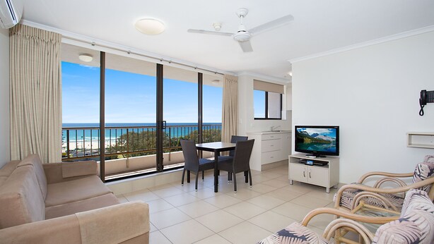 A spacious living area with a balcony overlooking the sea, a television, and a dining table with chairs. - Voyager Resort (Broadbeach)