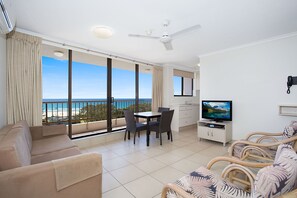 Amplia sala de estar con balcón vistas al mar, un televisor y una mesa de comedor con sillas.